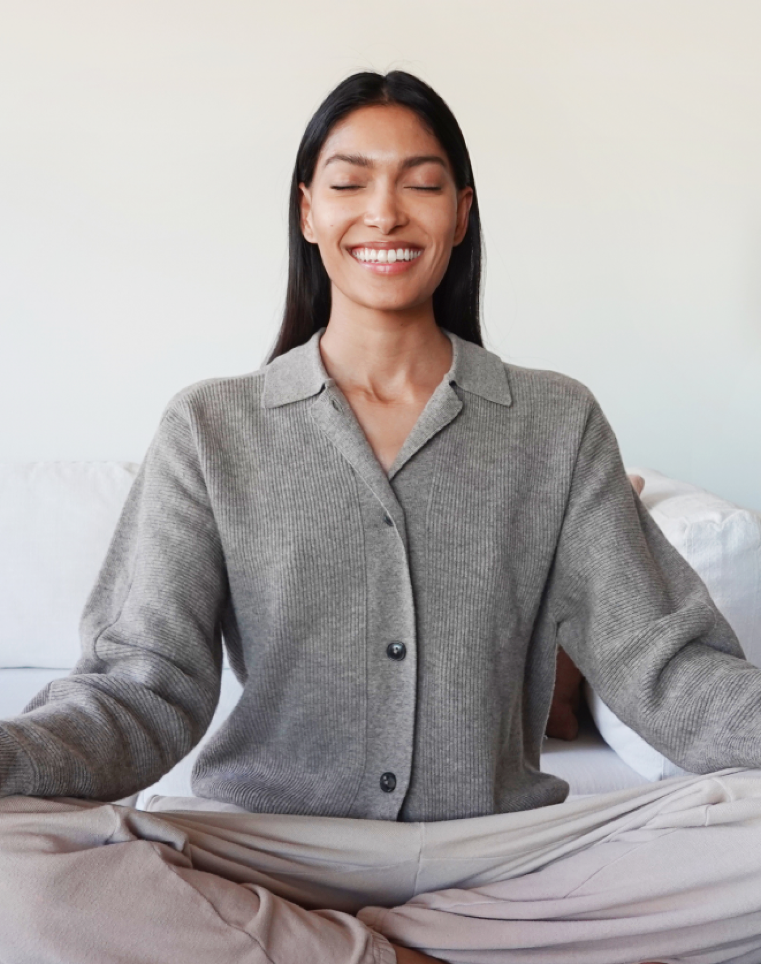 Woman practicing 2-1 breathing technique sitting cross-legged with eyes closed and smiling indoors