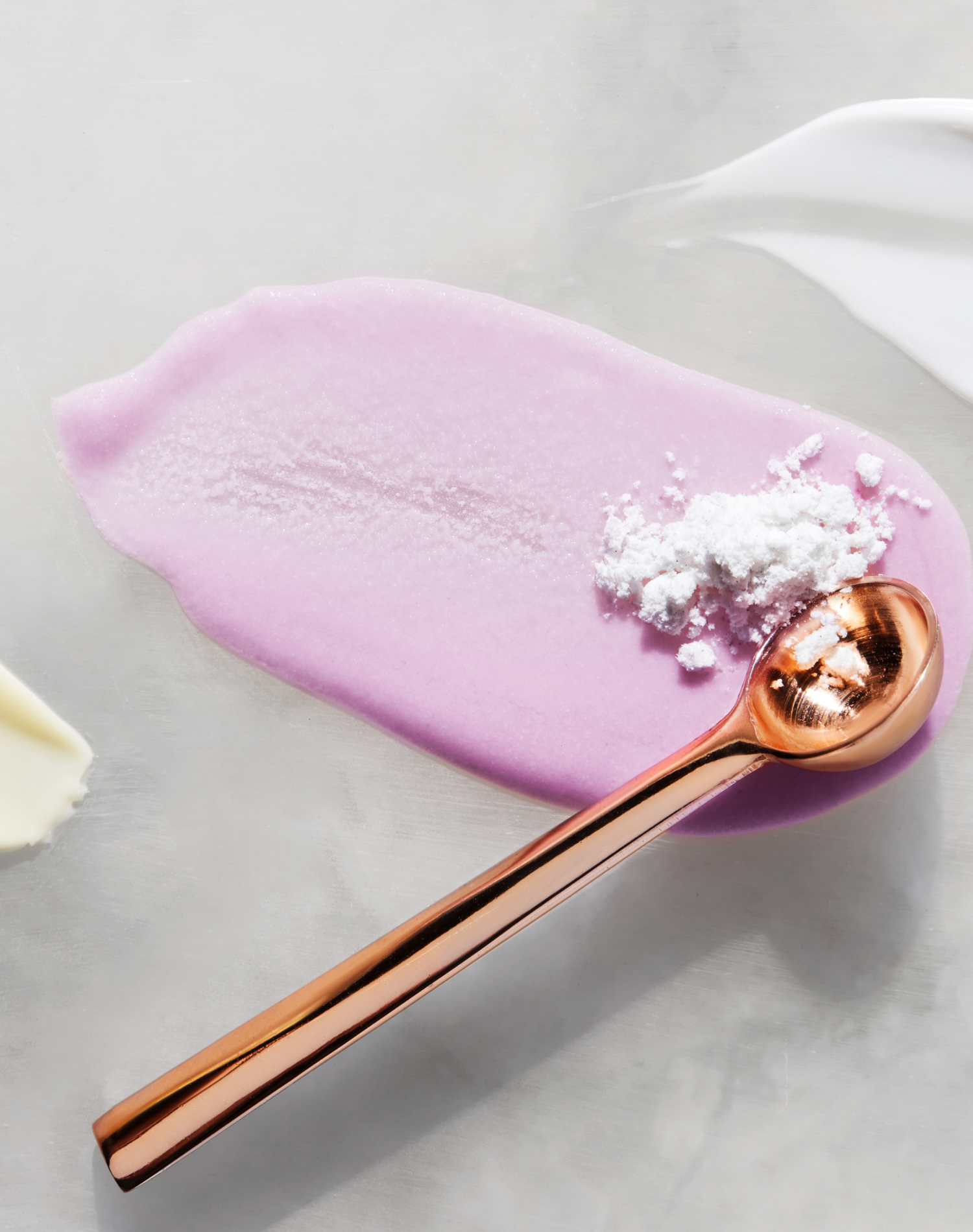 Copper spoon with white powder on purple and white clean beauty skincare product swatches on grey background