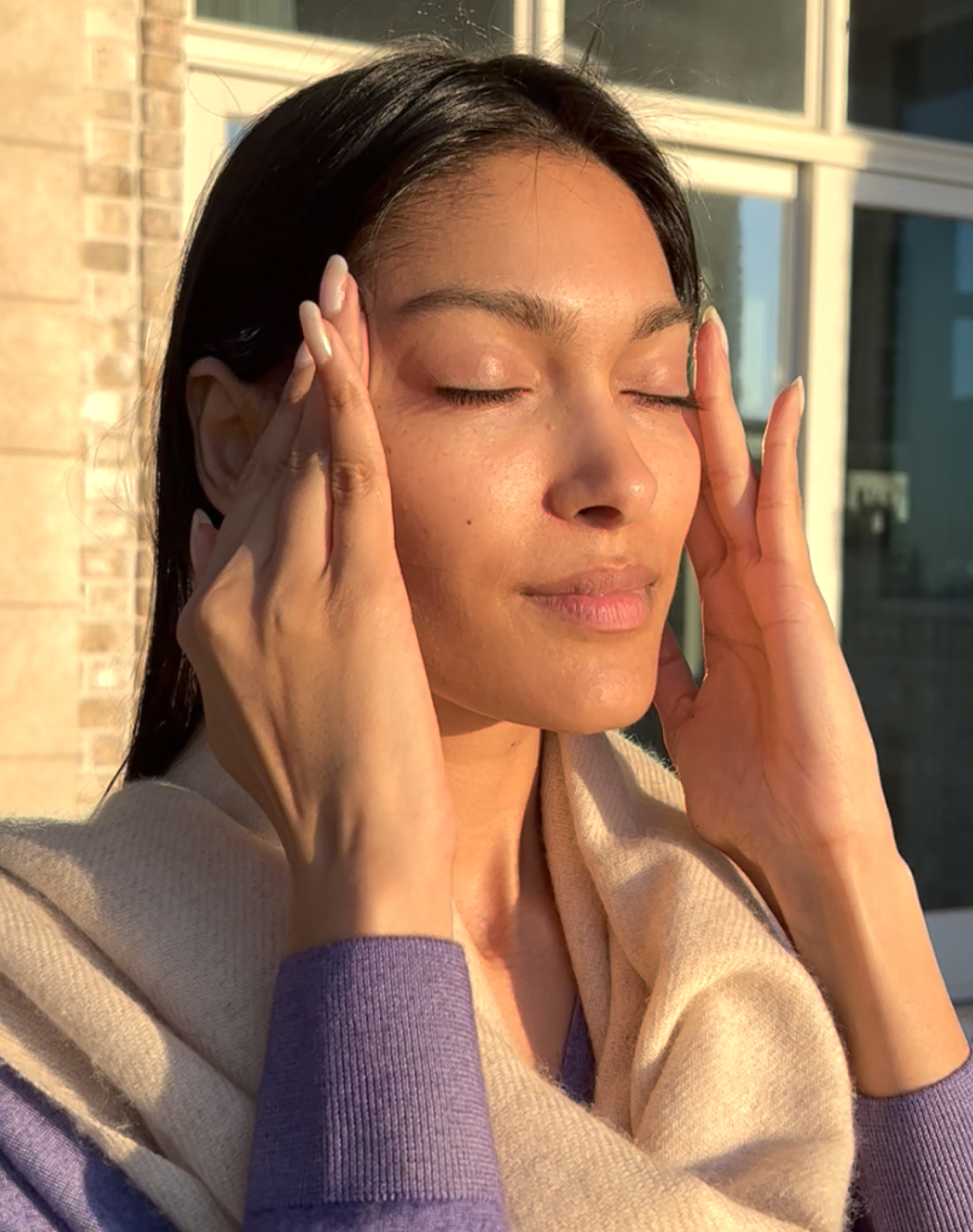 Woman performing Marma Facial Massage with closed eyes, gently pressing temples with fingers in natural light
