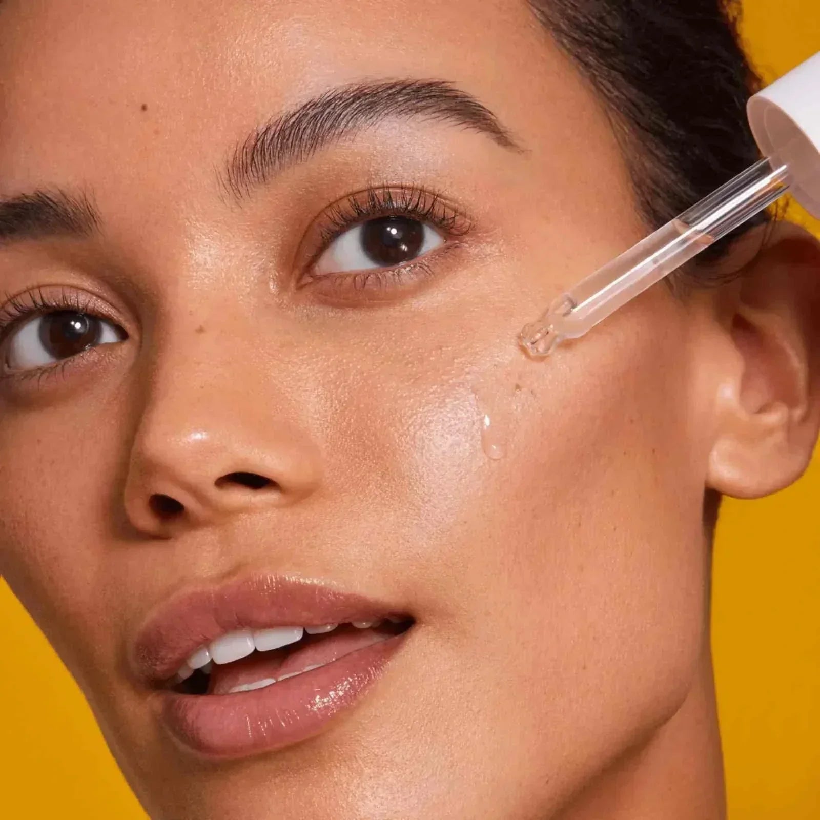 woman applying serum from skincare set to glowing skin on yellow background