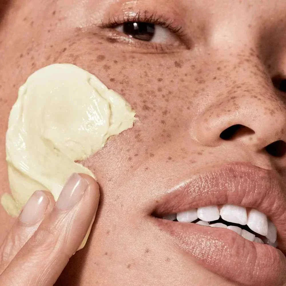 close-up of woman applying creamy mask on face showing skincare set effect and glowing skin