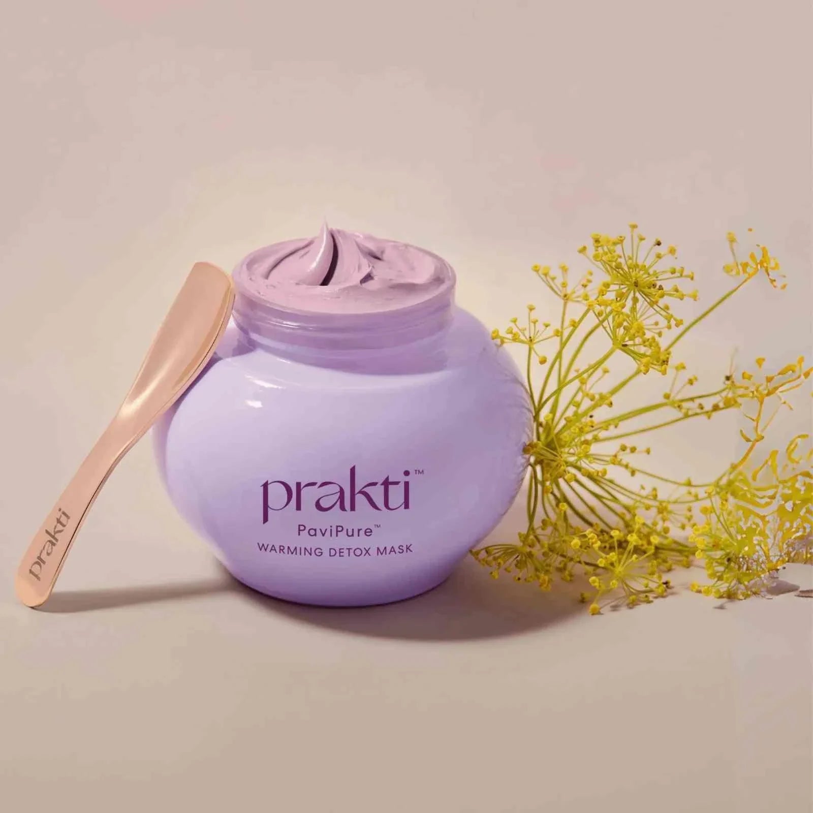 PaviPure warming detox clay mask in purple jar with wooden spatula and yellow flowers