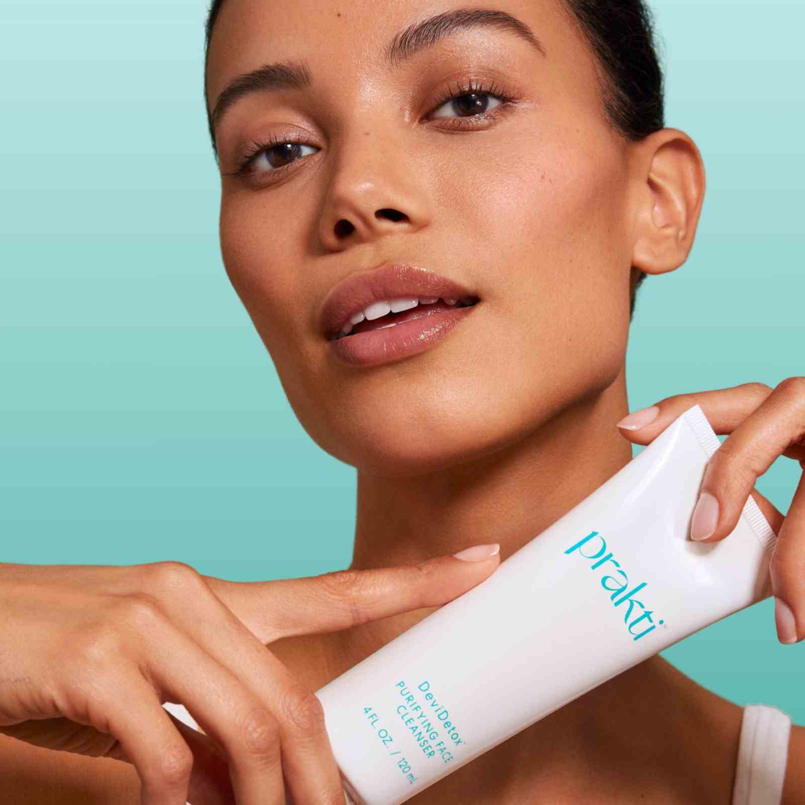 DeviDetox hydrating cleanser by Prakti held by woman with clear skin against blue background