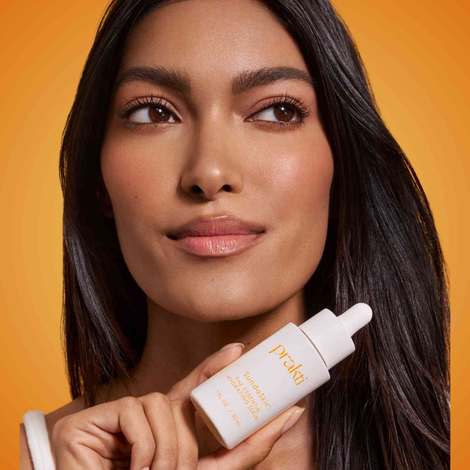 woman holding SundaSkin lightweight serum bottle with glowing skin on orange background